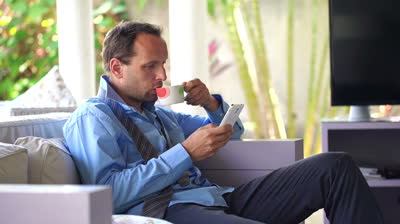 stock-footage-young-businessman-sitting-with-smartpone-and-drinking-tea-at-home